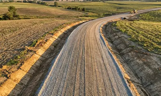 Engineered gravel driveway in North Missouri farmland with crowned surface, drainage ditches, and heavy equipment finishing work