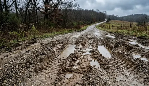 Failed gravel driveway with deep ruts, mud displacement, and water damage caused by clay soil in North Missouri