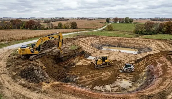 Excavator shaping and compacting clay basin during farm pond construction in North Missouri